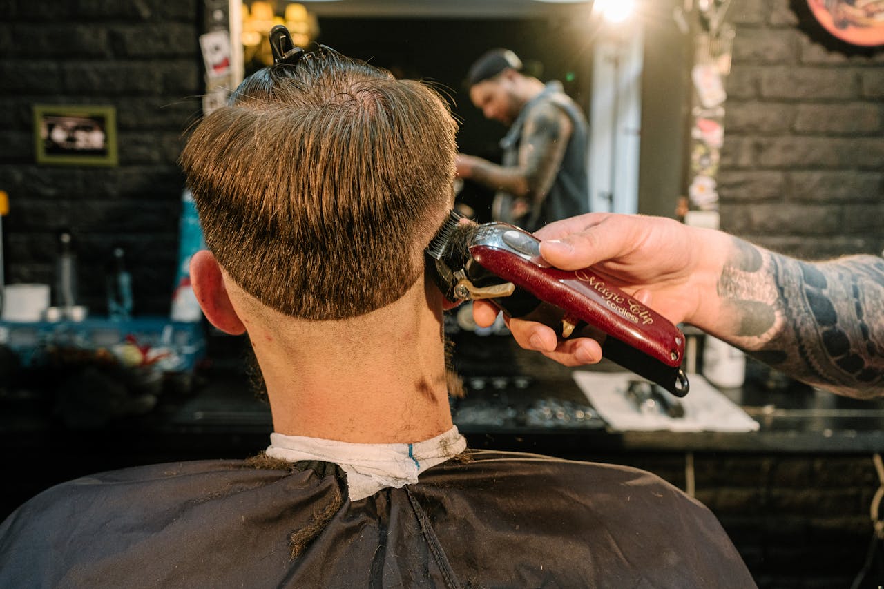 Back view of a man receiving a haircut with clipper in a barber shop.