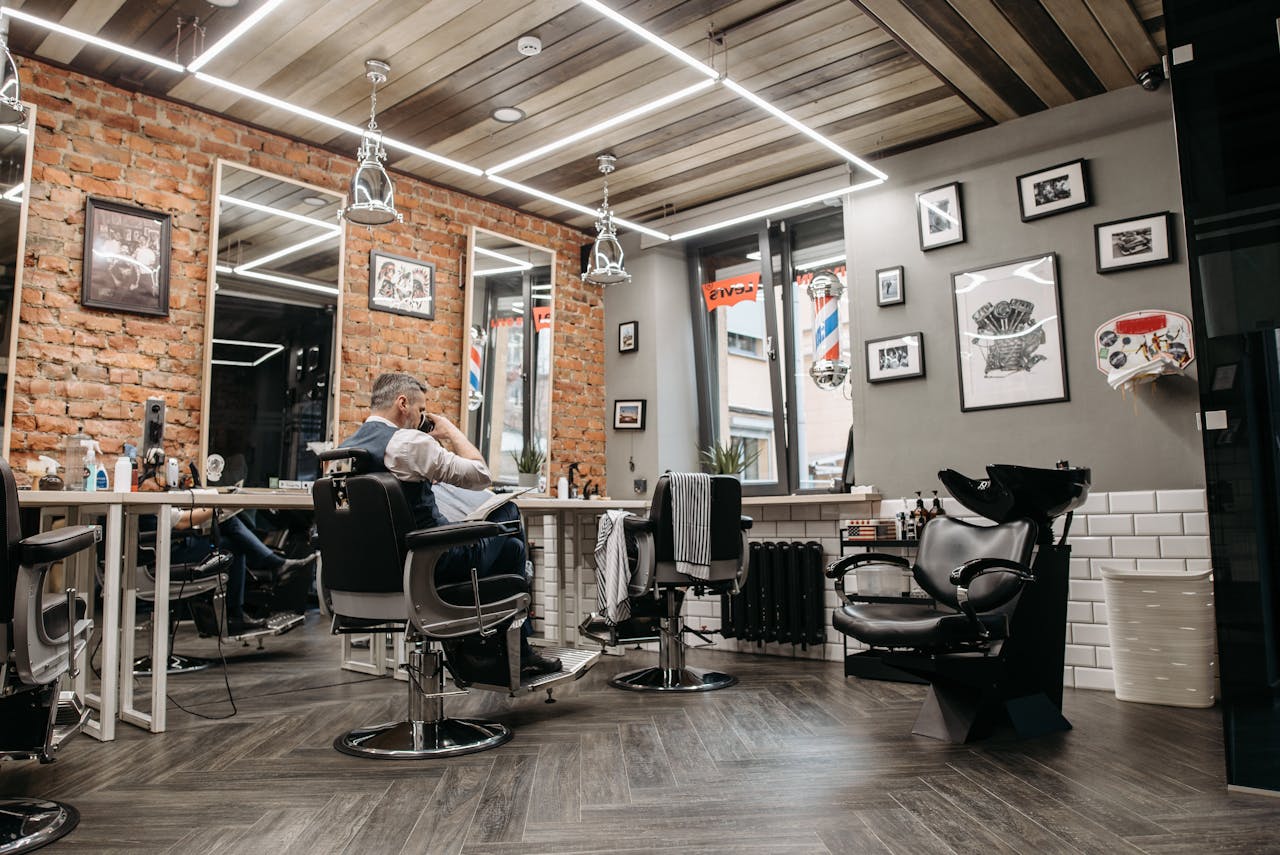 A sleek and stylish barbershop interior featuring upholstered chairs, mirrors, and customers.